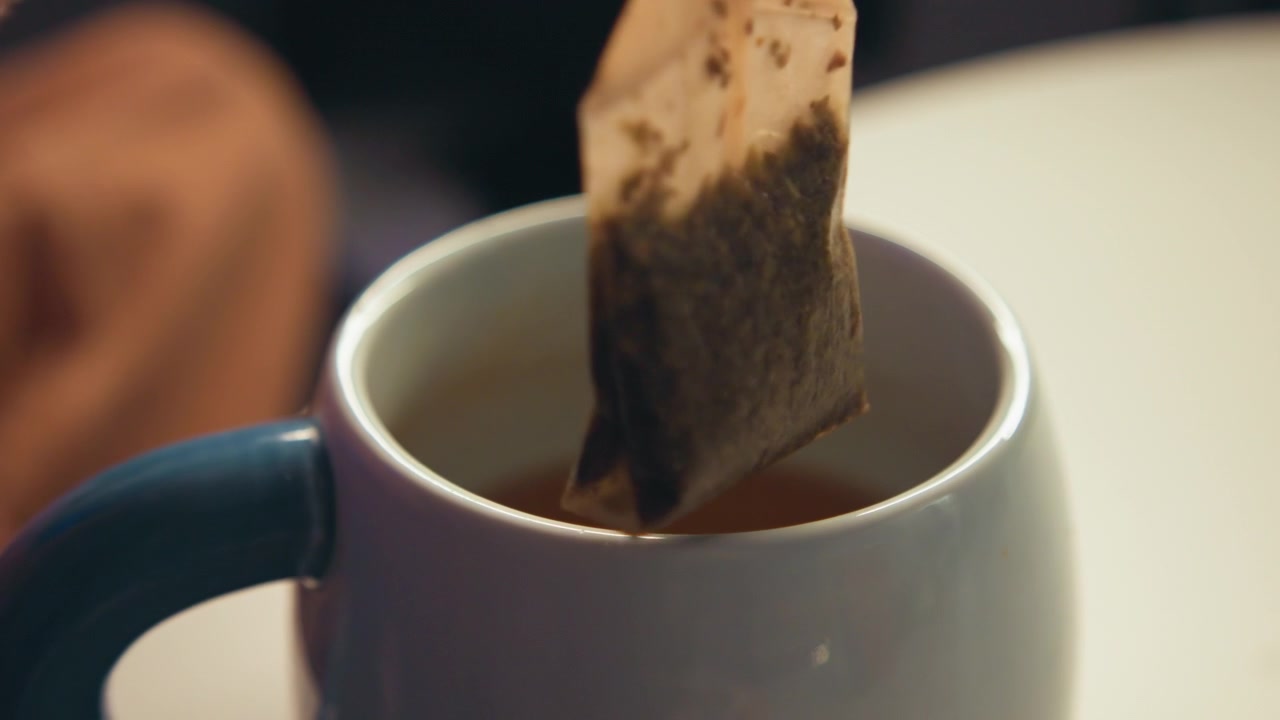 Primo piano di una tazza in ceramica piena di tè appena preparato dopo la rimozione della bustina di tè, vapore leggero, lievi increspature, colore ambrato caldo del liquido e un'accogliente ambientazione da tavolo che cattura la recente infusione e mescolatura.