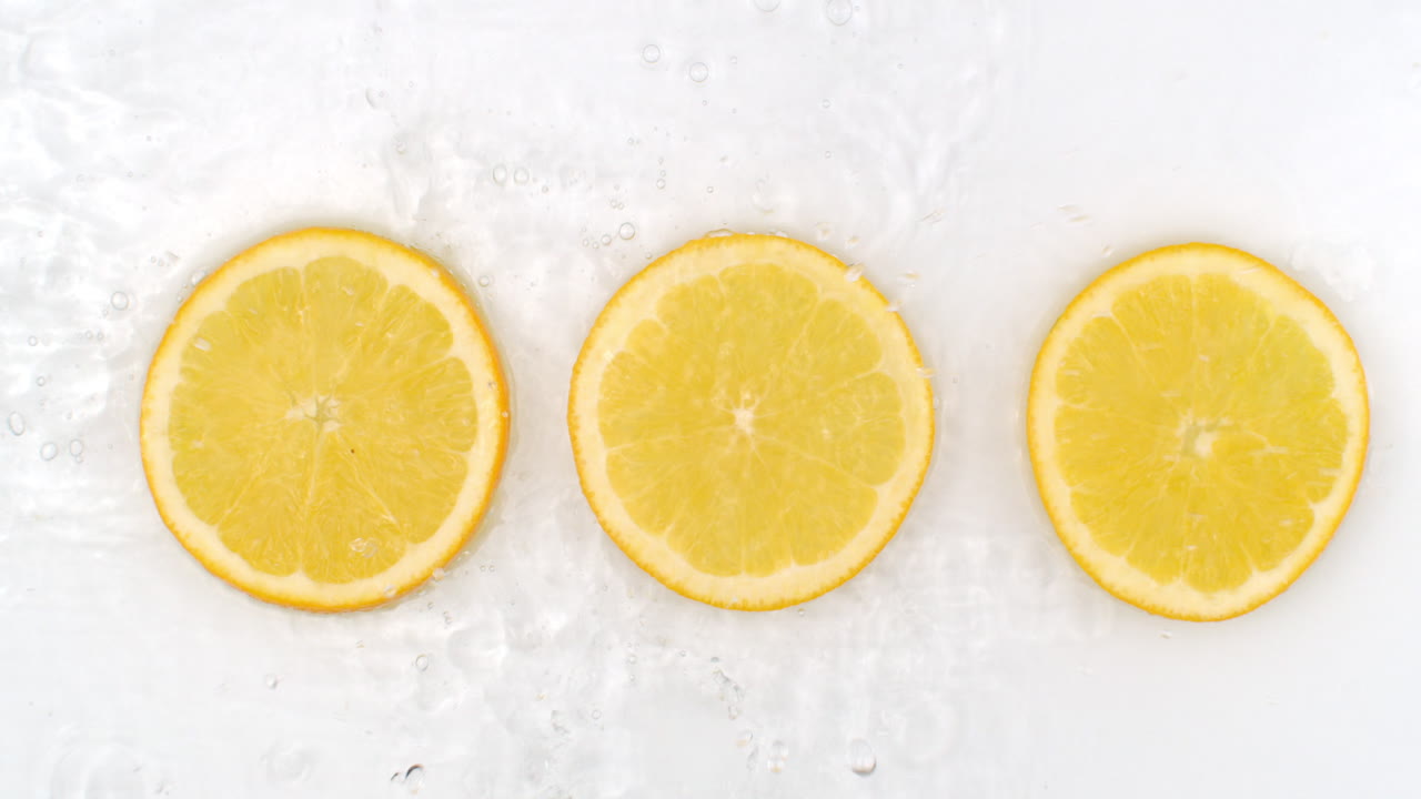 Slow motion water splash on three slices of orange lying on a white background in water