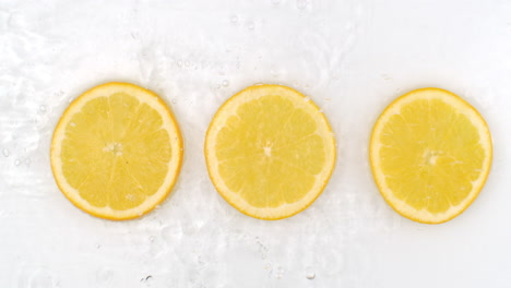 slow motion water splash on three slices of orange lying on a white background in water