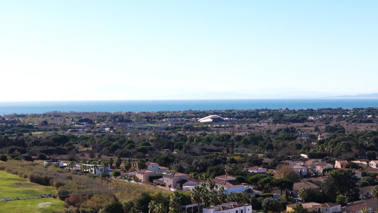 Luftfoto fra drone af Agde, Frankrig, med en golfbane og et moderne stadion. Middelhavslandskab med kysthorisont og boligudvikling