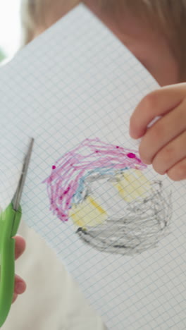 cute little boy cuts out color drawing of checkered paper in art classroom closeup. toddler child learns to use scissors at kindergarten lesson