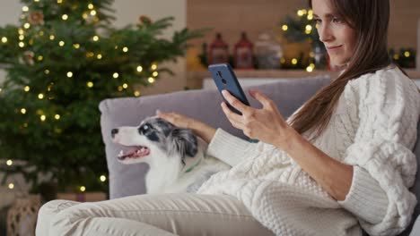 mujer relajándose con el perro en el sofá con teléfono móvil durante la navidad.