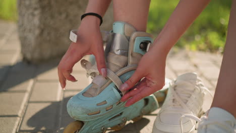 close-up of individual wearing black wristband adjusting strap on roller skate of right leg, with second roller skate slightly blurred in background and white sneakers nearby