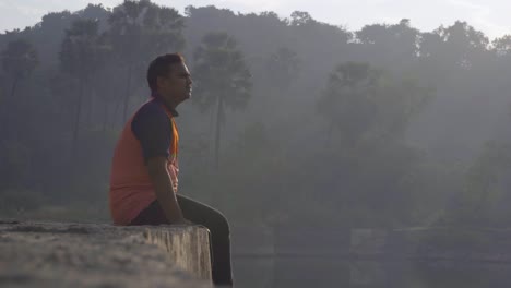 chico sentado en un muelle en el lago relajado disfrutando de la vista en la mañana del amanecer chico-hombre agua lago reavilling tiro reflejo en el agua primer plano destello de lente