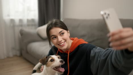 hermosa mujer tomando una foto selfie con un perro y sentada en el suelo en el interior de la casa