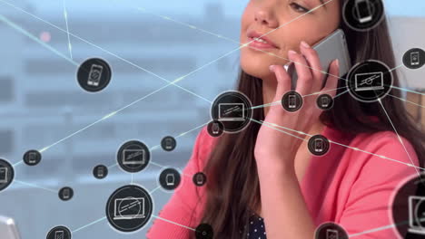 animación de iconos conectados sobre una mujer biracial sonriente haciendo una llamada mientras trabaja en una computadora portátil