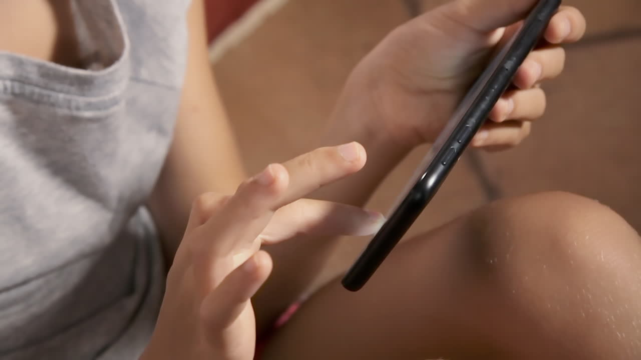 바닥에 앉아 있는 아이가 스마트폰을 사용하고, 화면에서 아이콘을 선택하고 만지고 있습니다.