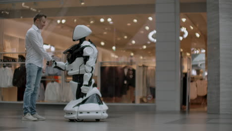 un hombre se para con un robot bot y le hace preguntas y pide ayuda haciendo clic en la pantalla en el cuerpo del robot. la interacción humano-robot en el mundo moderno