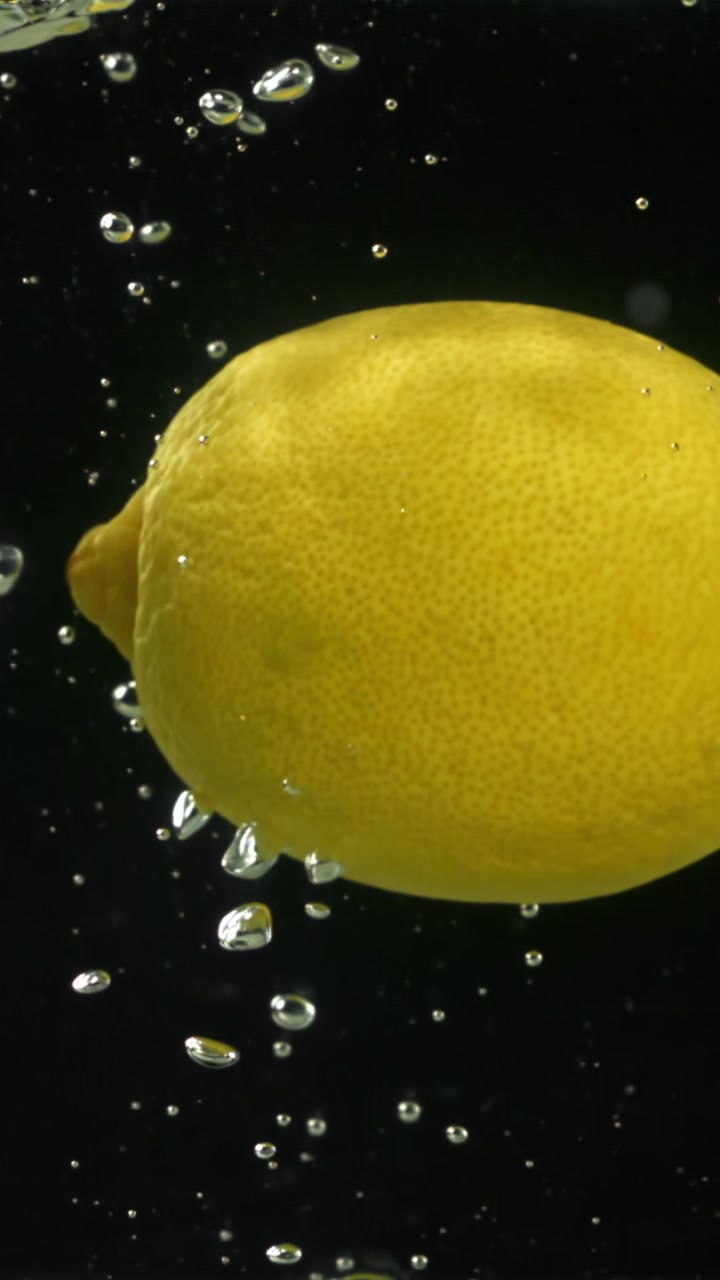 Limone giallo fresco sommerso nell'acqua con bolle che salgono