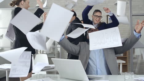 worker women and man dressed in suits at the office, they dance and celebrate while throwing documents