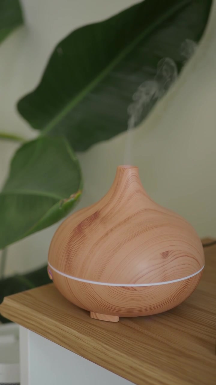 Diffuseur d'huiles essentielles en bois émettant de la brume sur fond de plante verte