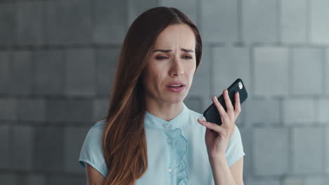 Upset-female-employee-recording-voice-message-on-cellphone-outside