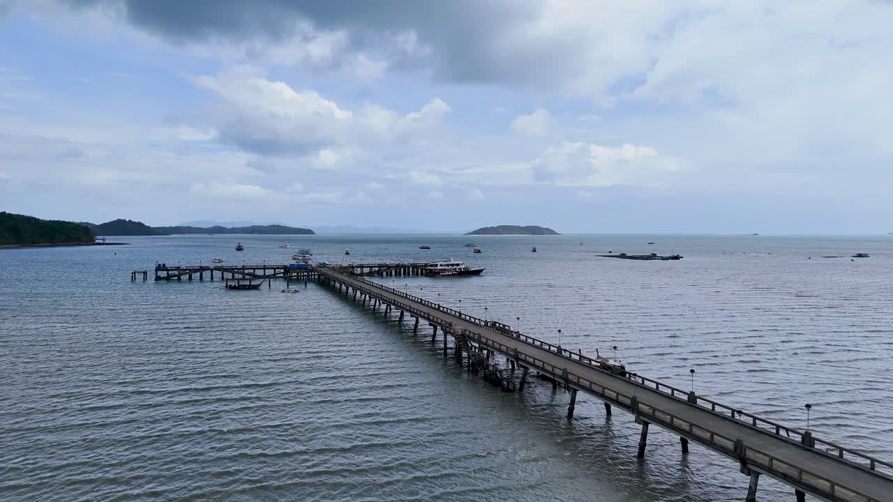 Drone footage captures a serene fishing pier in Phuket, Thailand, with calm waters and overcast skies, highlighting the tranquil coastal environment