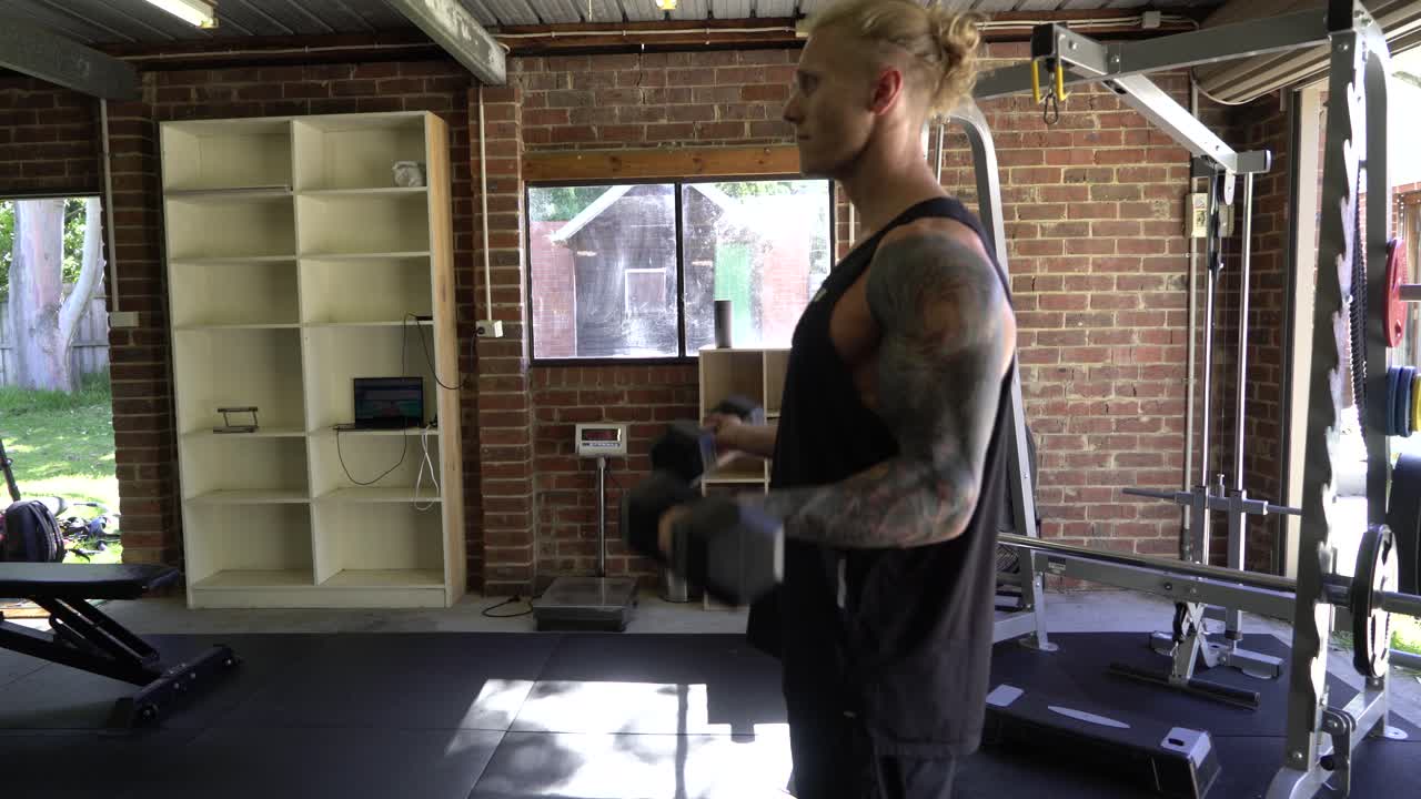 Tattoo man muscles in home gym doing bicep curls same time