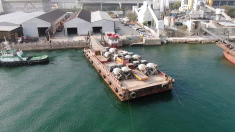 Barge-loaded-with-Concrete-mixer-trucks-pulled-to-port-by-a-Tugboat-in-Hong-Kong-bay,-Aerial-view