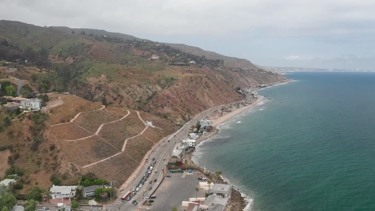 Aerial wide reverse pullback shot of the coastline near Duke's Malibu seafood restaurant along Pacific Coast Highway in Southern California. 4K