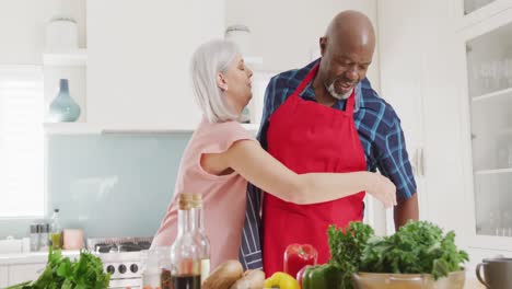 Happy-senior-diverse-couple-wearing-aprons-in-kitchen