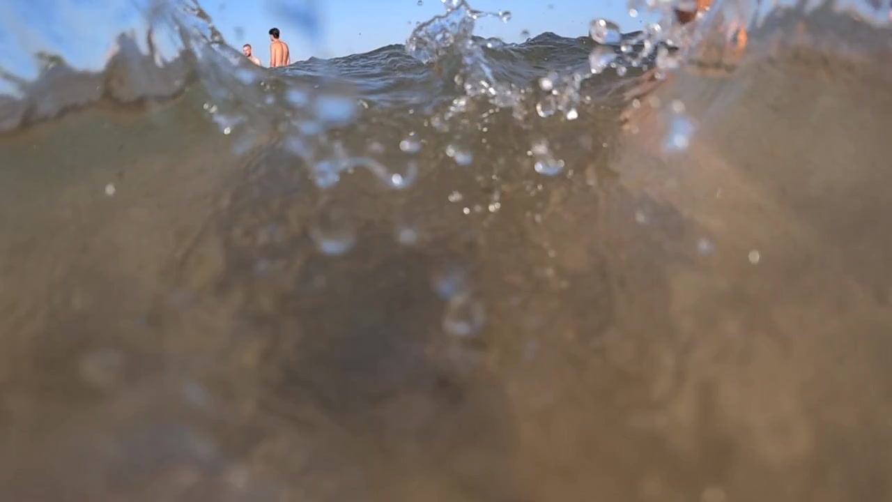 Water splashing and overflowing against a clean blue sky, creating a dynamic surface and bright droplets
