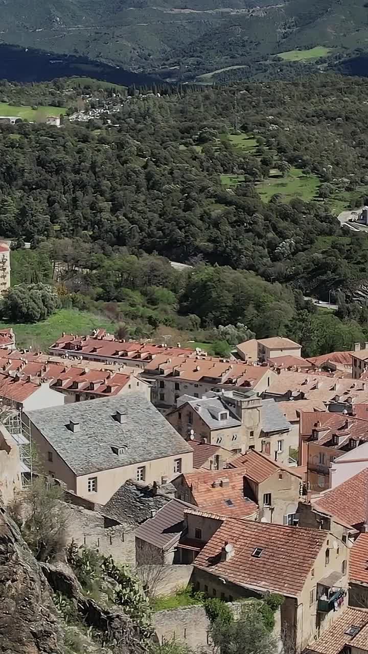 Vista di un villaggio in Corsica con edifici su scogliere rocciose e montagne