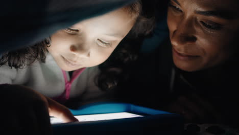 madre e hija felices usando una tableta bajo una manta jugando juegos en la tecnología de pantalla táctil relajándose divirtiéndose antes de acostarse