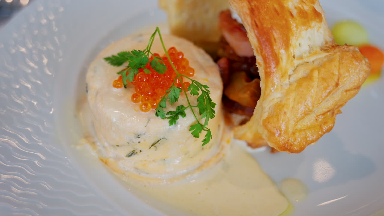 Close up of a fish mousse with salmon roe and puff pastry on a white plate at a restaurant