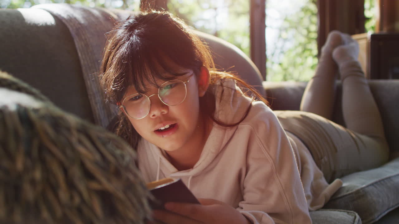 집에서 소파에 앉아서 책을 읽는 동안 미소 짓는 아시아 소녀