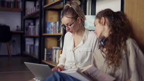 two smiling female college students learning together and reading books in university library on the floor