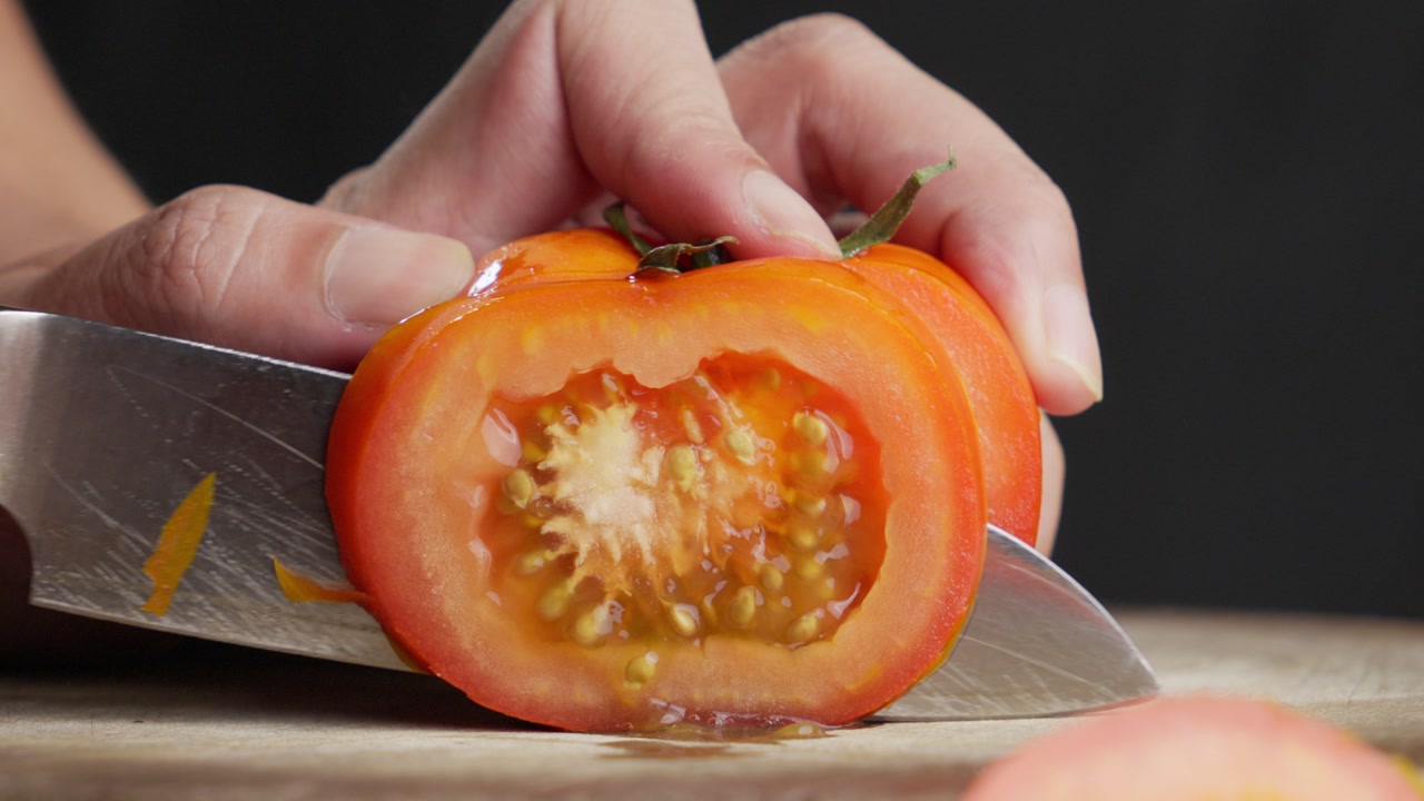 Slicing a tomato with a scratched kitchen knife. Slow-motion close-up