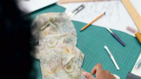 top view of woman tailor sitting on table cutting clothes pieces in sewing workshop