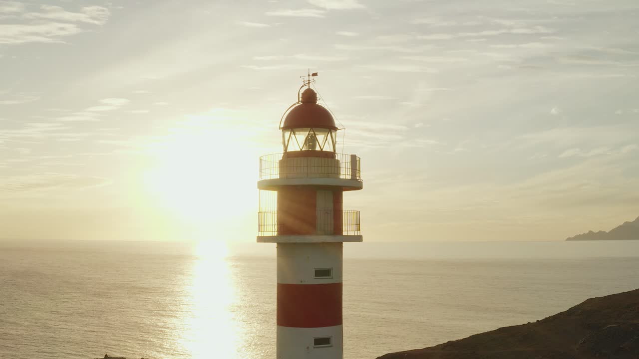 toma cercana de un faro con sol y océano en el fondo a la hora dorada