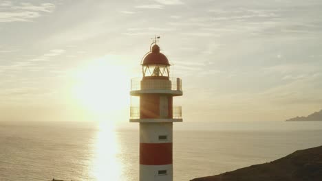 Close-drone-shot-of-a-lighthouse-with-sun-and-ocean-in-the-background-at-golden-hour