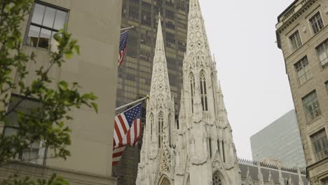 a wide panning shot of american flags waving among manhattan’s office buildings, with cathedral rooftops visible in the background. captured in new york city. a historic and urban skyline.