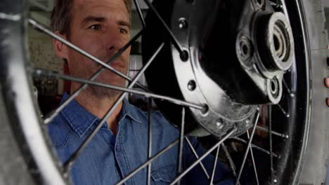 male mechanic examining motorcycle wheel in repair garage 4k