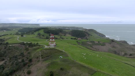 Drone-flyover-toward-to-Antenna-landmark-on-hilltop-of-Cape-Quejo-fields,-Cantabria