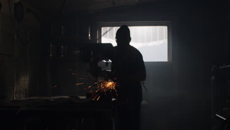 masked person grinds metal with an angle grinder throwing sparks over their metal shop