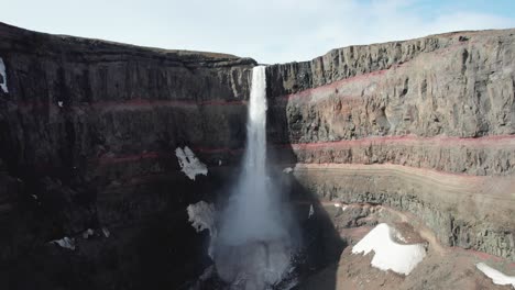 fotografía aérea del pedestal de la cascada de hengifoss en el este de islandia, mostrando sus columnas de arcilla roja y basalto