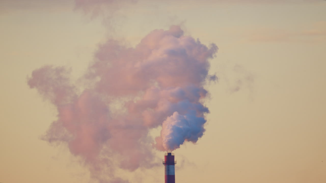 Ciminiera industriale che rilascia fumo denso nel cielo sopra un cantiere edile cittadino.