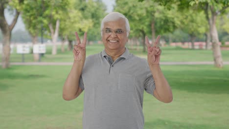 Happy-Indian-old-man-showing-victory-sign-in-park