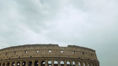upper section of the ancient colosseum, with its iconic arches and a traditional street lamp, set against a cloudy sky