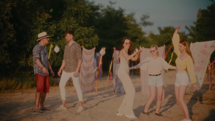 беспечные женщины танцуют рядом с мужчинами, разговаривающими на пляже.