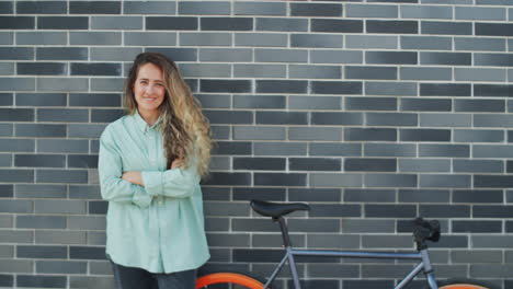 cheerful woman standing by bike on street and posing for camera