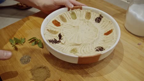 decorating hummus dish with cumin, paprika, rosemary spices by hand