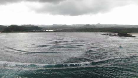 aerial pullback on gloomy day, passing over surfers waiting for waves off of tanjung aan beach, lombok