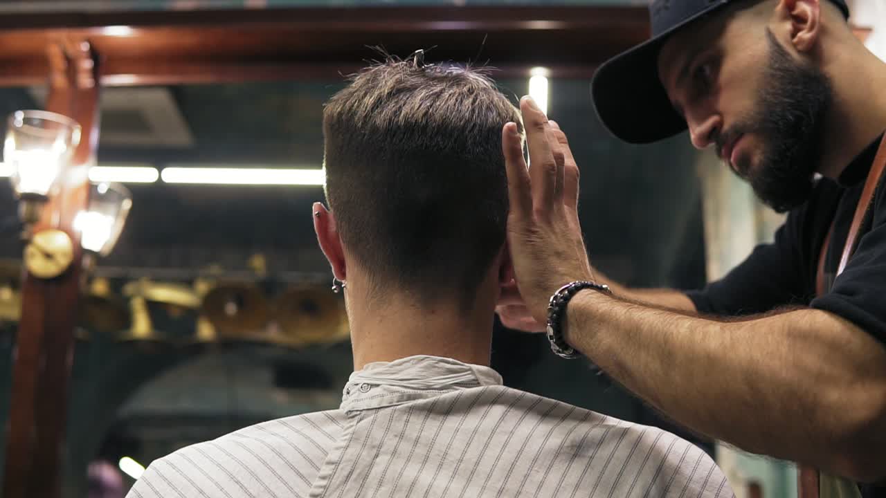 Back view of a young man getting his haircut sitting in the chair at the barber shot. Barber cuts the hair of the client with