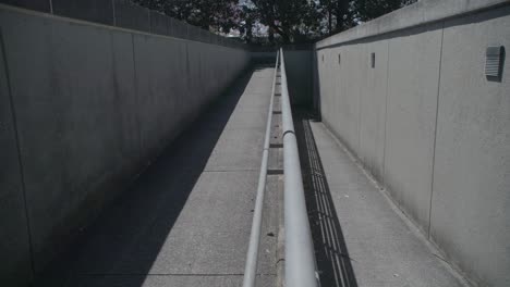 the image features a narrow, concrete pedestrian ramp flanked by high walls, converging in a vanishing point perspective