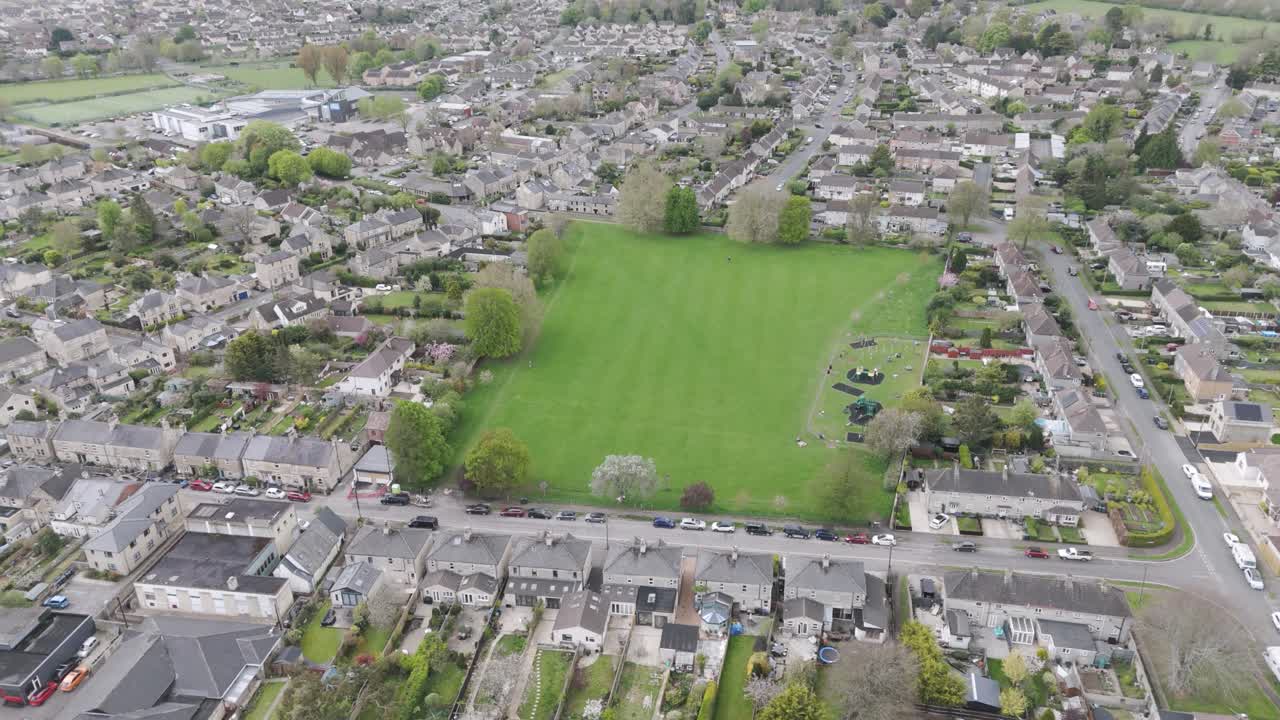 Top-down aerial of vibrant rectangular recreation ground “The Rec” bordered by stone houses, tree-lined footpaths and residential streets in Corsham