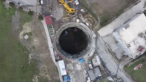 workers climb up a lattice ladder while excavators excavate in deep tunnel shaft construction.