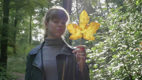 beautiful young woman gazes at yellow leaf in forest, lens flare