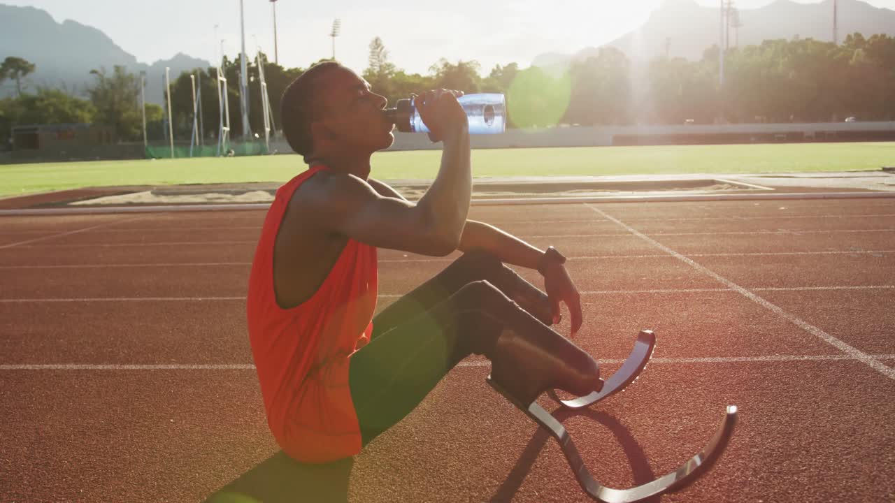 Uomo di etnia mista con disabilità e protesi alle gambe seduto sulla pista di atletica