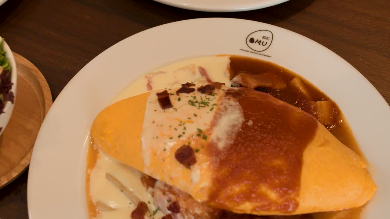 Camera pans over Japanese omelette rice as sauce changes, with salad and soup sides visible